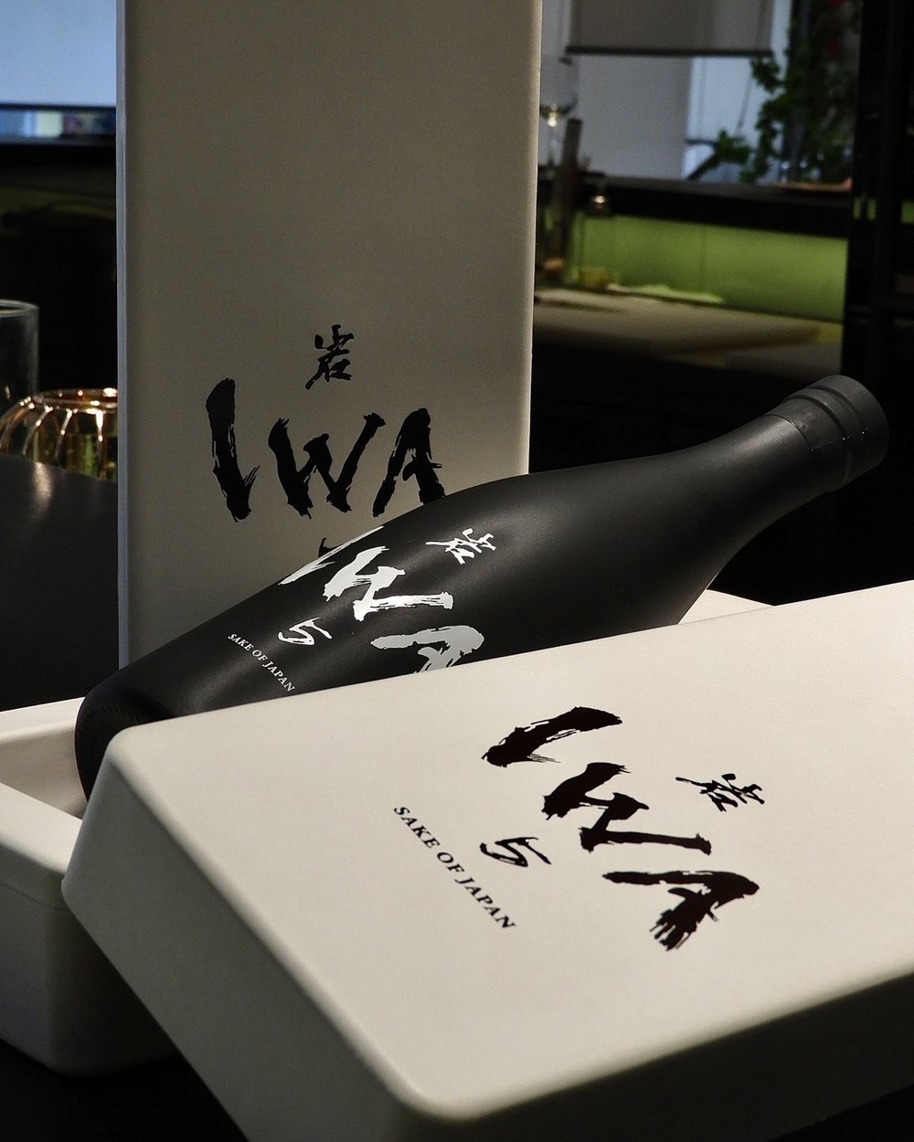 A matte black bottle of IWA5 sake resting in its presentation box.