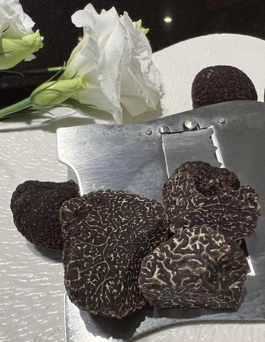 Fresh black truffles, halved to show their marbled interior, beside white roses.