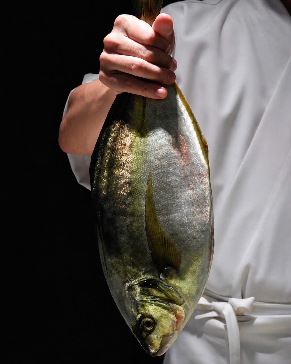 A chef holding a whole striped jack, fresh from the market.