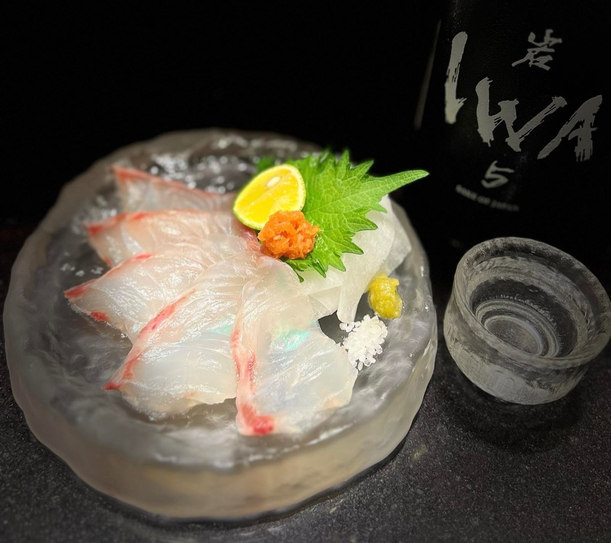 Sashimi cá bơn phục vụ trên khối đá cùng rượu sake, trang trí với tía tô, cam chanh và trứng cá hồi.