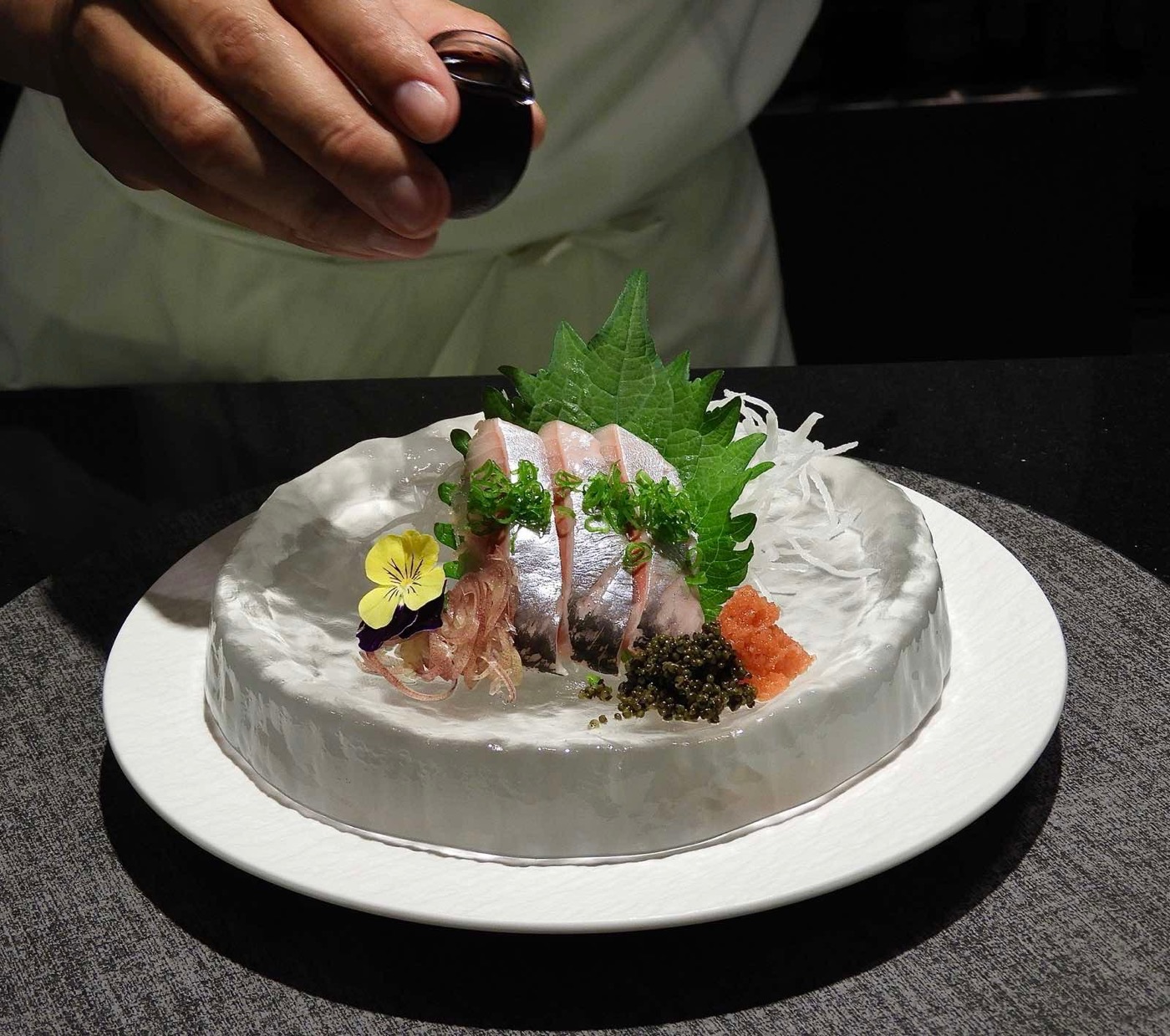 Đầu bếp rưới nước sốt lên sashimi cá bơn bày trên đá.