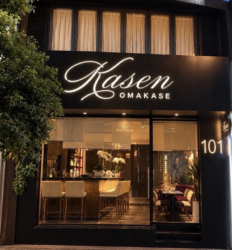 Kasen's renovated storefront at dusk, glass entrance lit beneath the illuminated Kasen Omakase sign at 101 Lê Thị Riêng.