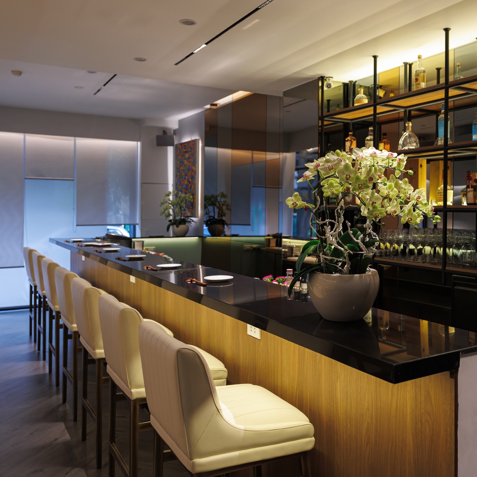 Kasen's ten-seat omakase counter with orchids and illuminated bottle shelves.