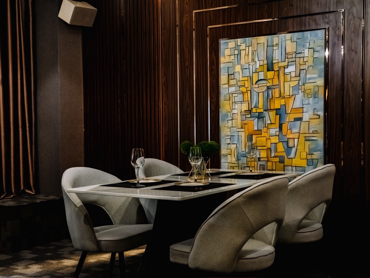 A corner of the private room, a large abstract painting on the wall behind wine glasses set at the table.