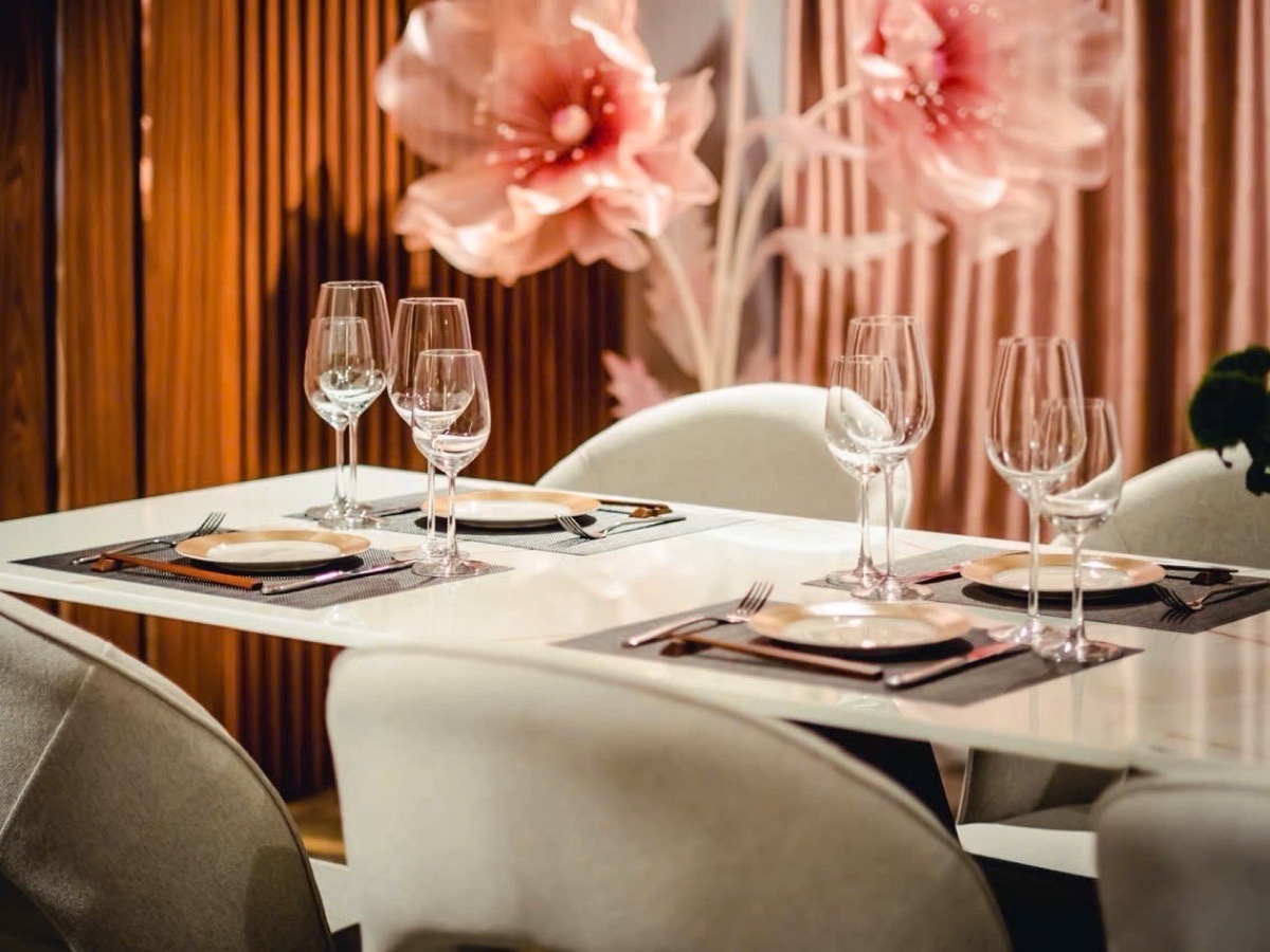 A table set beneath oversized paper blossoms against a pleated amber curtain.